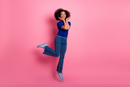 Happy young woman with curly hair jumping against pink background showcasing vibrant style and...