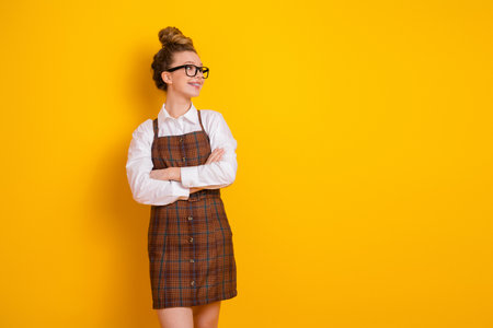 Smiling young woman in stylish attire poses against vibrant yellow background, expressing confidence and charmの写真素材