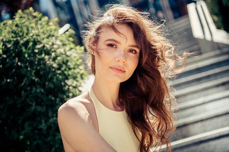 Young brunette woman enjoying a sunny day outdoors wearing a yellow dress with stylish hairstyle and...