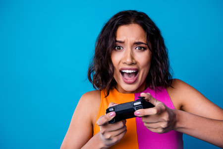 Cheerful woman intensely focused on gaming with a thrilling expression against a vibrant blue...