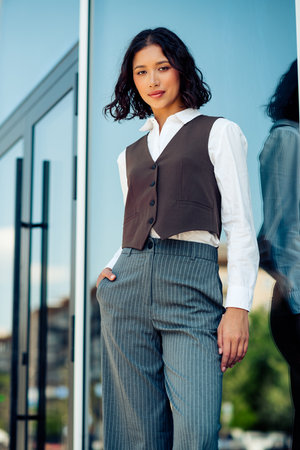 Confident young businesswoman outdoors in stylish formal wear, standing by a modern glass building in an urban cityscapeの写真素材