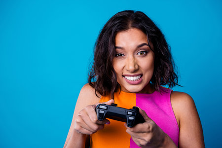 Young fashionable woman holding a game controller with an expressive look on a colorful vibrant blue backgroundの写真素材