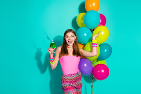 Young woman in colorful retro attire celebrating with balloons against turquoise backgroundの写真素材