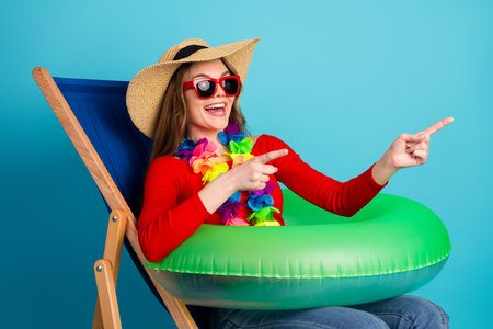 Cheerful young woman in summer attire enjoying leisure time with inflatable ring and colorful...
