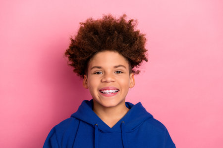 Happy teenage boy smiling joyfully in blue hoodie against bright pink background showcasing style and confidenceの写真素材