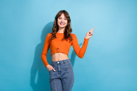 Young woman in orange top modeling confidently, posing against a blue background, showcasing casual style and fashionable gestures.の写真素材