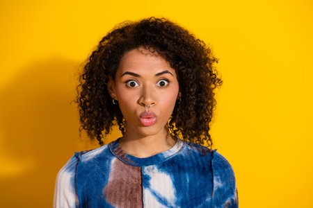 Portrait of a surprised young woman wearing a colorful top against a vibrant yellow backgroundの写真素材