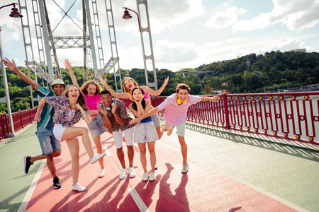 Group of cheerful young friends enjoying a sunny day on a scenic urban bridge celebrating friendship...