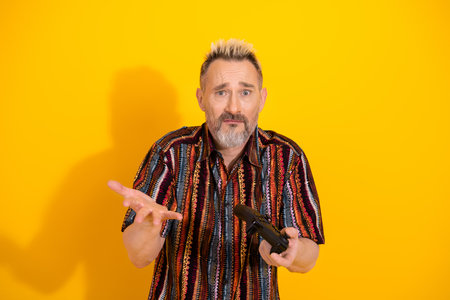 Charismatic bearded man in colorful shirt expressing curious gesture against vibrant yellow studio...