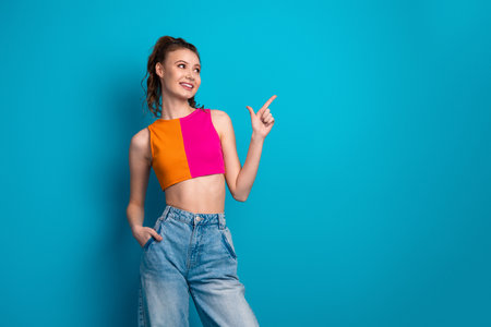 Young woman in vibrant outfit posing against blue background with cheerful expression and confident...