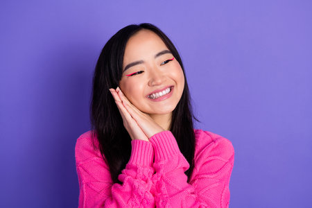 Cheerful young woman in bright pink sweater smiling happily against vibrant purple background, showing stylish fashion and joyful energyの写真素材