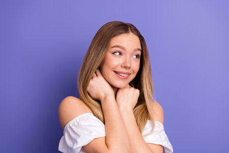 Charming young woman smiling with a cheerful expression wearing a stylish white top against a vibrant purple background.の写真素材