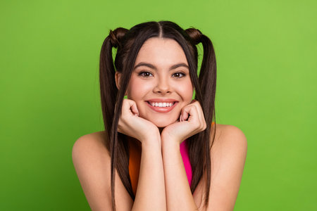 Bright young woman with trendy ponytails posing against a vibrant green background exuding...