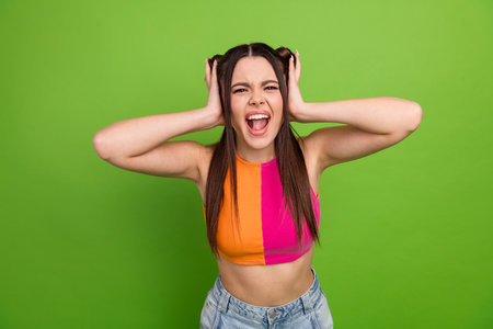 Cheerful young woman with vibrant outfit expressing excitement against a vivid green backdropの写真素材