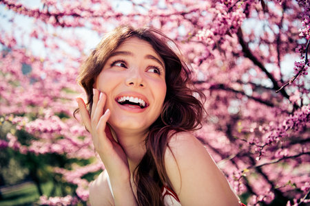 Lovely woman enjoying a sunny day in a blooming garden with pink flowers, smiling joyfully and embracing the outdoor sceneryの写真素材