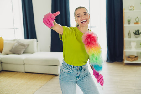 Happy young woman cleaning her living room with a colorful duster in a joyful mood