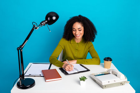 Young woman enjoying her tasks at a creative workspace with vibrant blue background and modern casual styleの写真素材