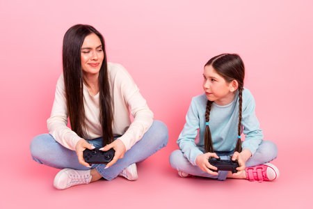 Mother and daughter bonding over a gaming session against a pink pastel background, enjoying quality time togetherの写真素材