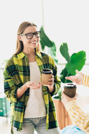 Young woman enjoying coffee indoors while discussing with a colleague in a bright modern coworking spaceの写真素材