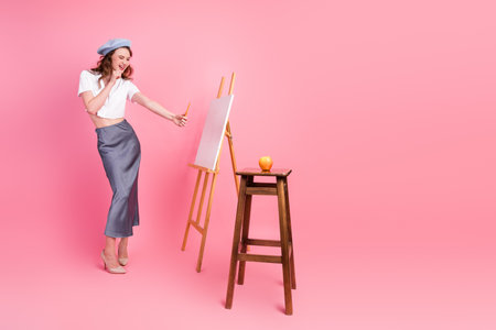 Youthful woman artist sketching on a canvas with a playful demeanor in a pink studio setting with balanced propsの写真素材