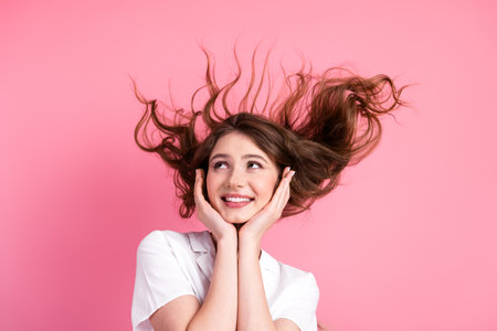 Portrait of a cheerful young woman with flowing brown hair, smiling brightly against a vibrant pink backgroundの写真素材