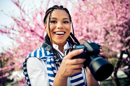 Cheerful young woman enjoying photography in blooming park, showcasing a carefree lifestyle and...