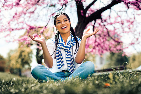Cute woman enjoying a sunny spring day outdoors under blooming trees in a city park with a joyful smileの写真素材