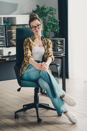 Young female programmer working on a computer at a home office workspace, wearing glasses and casual...