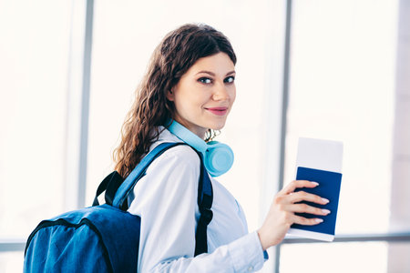 Charming woman with blue backpack holding a passport confidently in a modern airport, ready for an...
