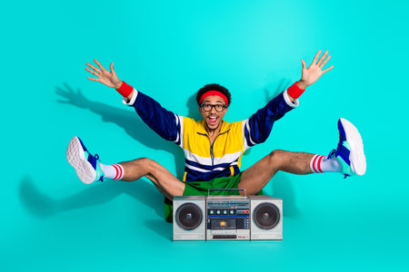 Energetic young man with a retro boombox in vibrant activewear on a bright teal background embodying fun and sporty style leisureの写真素材