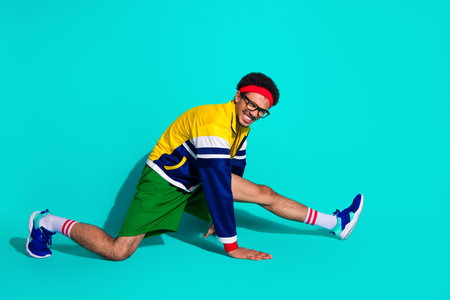 Energetic male athlete in retro outfit stretching with a vivid teal background showcasing a fun and dynamic sporty lifestyle vibeの写真素材