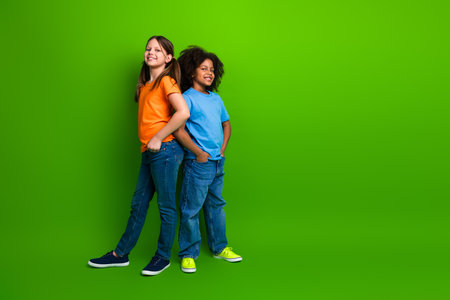 Happy and diverse preteen girls standing together in casual outfits against a vibrant green background with joyful smilesの写真素材