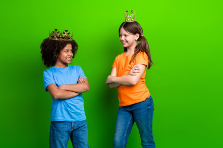Cheerful children wearing crowns standing against a bright green background representing happinessの写真素材