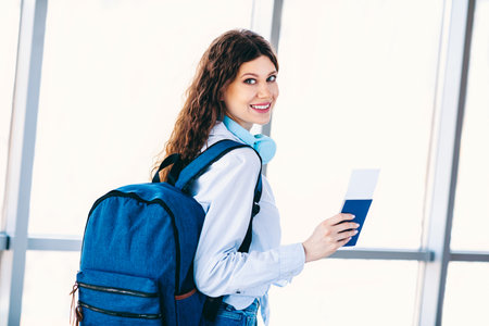 Young female traveler with backpack and boarding pass preparing for a journey at an airport terminalの写真素材