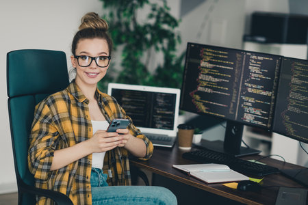 Young female programmer working remotely in her home office with coding screens, laptop, and a professional workspace environmentの写真素材
