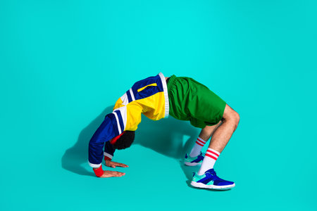 Young male athlete in a vibrant retro sports outfit performing exercise against a teal backgroundの写真素材
