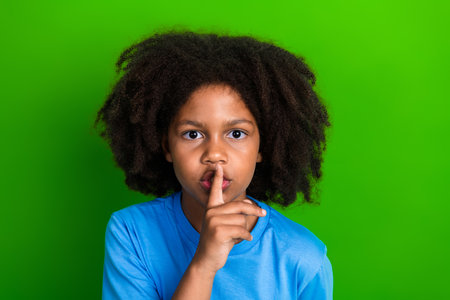 Smiling child with hush gesture against a green background, promoting quietness, calmness, and attentionの写真素材