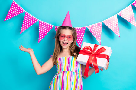 Joyful preteen girl in party attire celebrating with gift box and festive decorations against a...