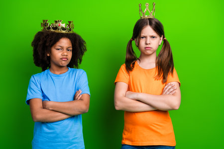 Two schoolgirls wearing playful crowns pose confidently with crossed arms against a bright green backgroundの写真素材