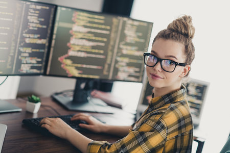 Young female programmer working on multiple monitors coding software at a stylish workspace in a modern home officeの写真素材