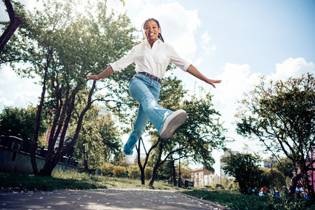 Cute woman joyfully jumping in a park during a beautiful spring day, radiating happiness and energy with green surroundingsの写真素材
