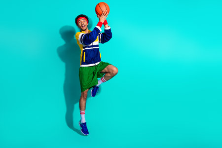 Energetic young man playing basketball in retro sports attire against a bright turquoise background,...