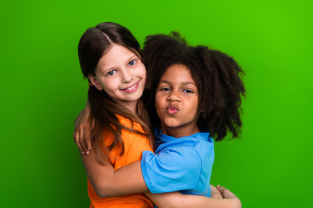 Charming young friends hugging on green background in casual clothing, depicting joy, childhood and togethernessの写真素材