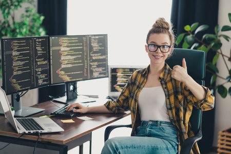 Confident young female programmer giving thumbs up while working on coding projects at her home...