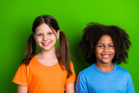 Smiling schoolgirls standing together against green background promoting friendship and diversity with vibrant casual styleの写真素材