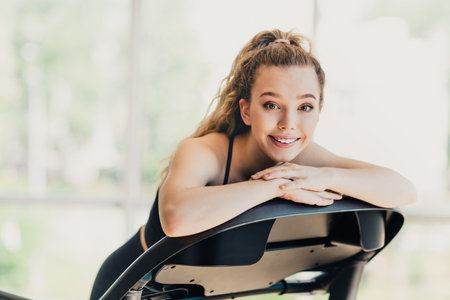 Athletic Energetic Woman Exercising Indoors on Treadmill in Modern Fitness Setting, Smiling with Confidence and Fitness Goalsの写真素材