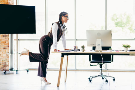 Confident businesswoman working at office desk, standing and reviewing project on desktop computer in modern sunlight interiorの写真素材