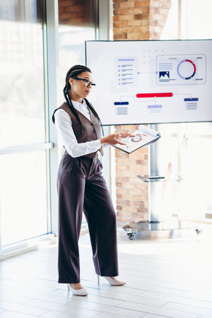Professional businesswoman giving a presentation in a modern office with visual analytics displayed...