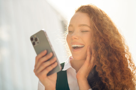 Confident young businesswoman enjoying leisure outdoors with smartphone during a sunny day in the cityの写真素材