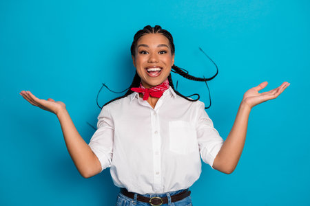 Charming young woman with joyful expression wearing casual outfit and red scarf against bright blue...